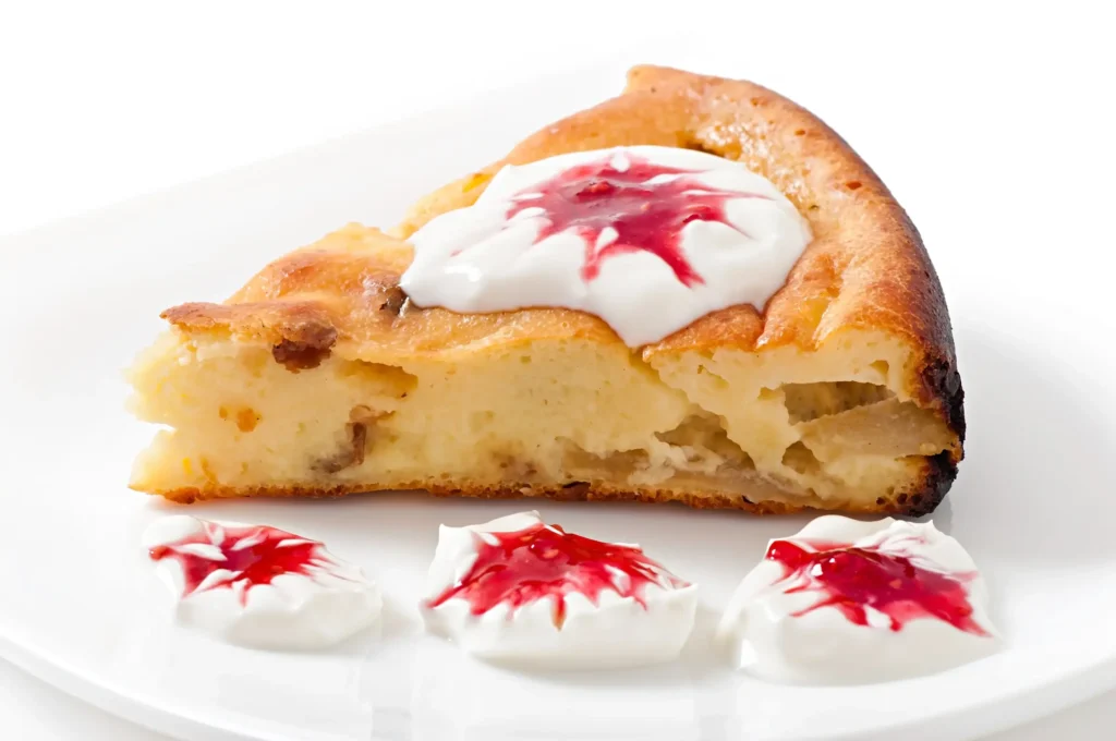 A slice of bread pudding topped with whipped cream and raspberry jam on a white plate.