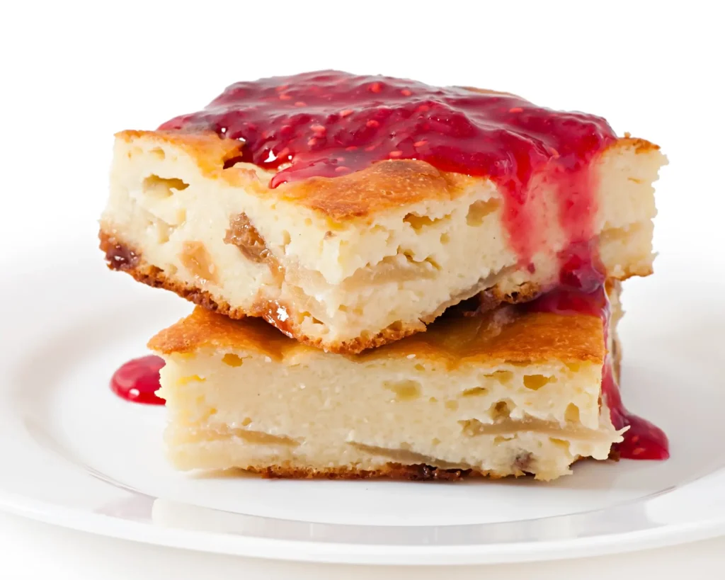 Two stacked slices of bread pudding topped with raspberry jam on a white plate.