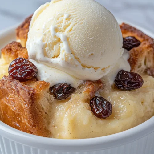 Warm bread pudding in a white ramekin topped with a scoop of vanilla ice cream and raisins.