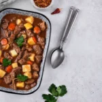 A rectangular dish filled with hearty beef goulash, featuring tender beef chunks, potatoes, carrots, and a rich brown sauce, garnished with fresh parsley.