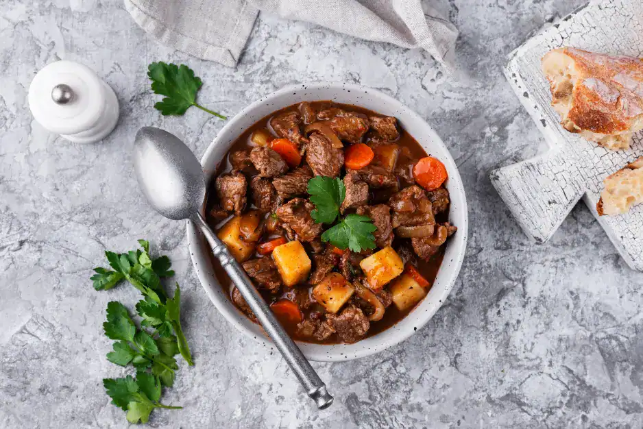 A bowl of hearty beef goulash filled with tender beef chunks, carrots, potatoes, and rich broth, garnished with fresh parsley, served with crusty bread.