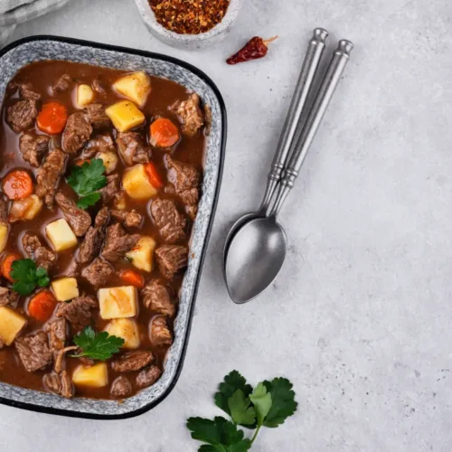 A rectangular dish filled with hearty beef goulash, featuring tender beef chunks, potatoes, carrots, and a rich brown sauce, garnished with fresh parsley.