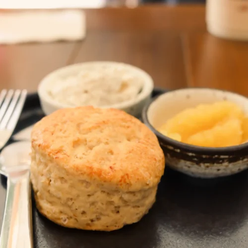 Freshly baked traditional English scone served on a black plate with clotted cream and jam in small bowls.