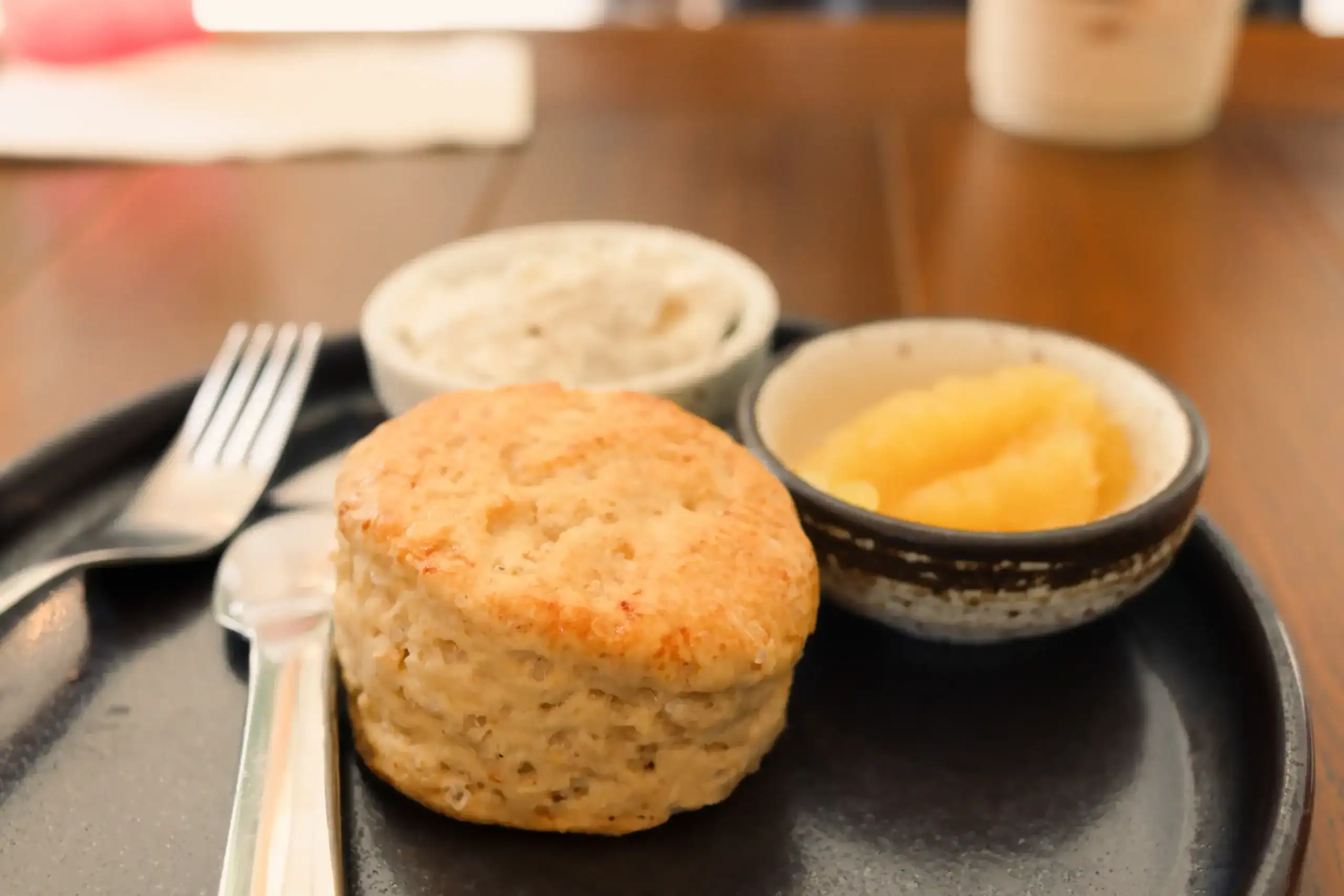 Freshly baked traditional English scone served on a black plate with clotted cream and jam in small bowls.