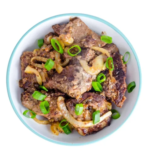 A top view of a bowl filled with cooked beef liver and caramelized onions, garnished with fresh green onion slices, set against a white background.