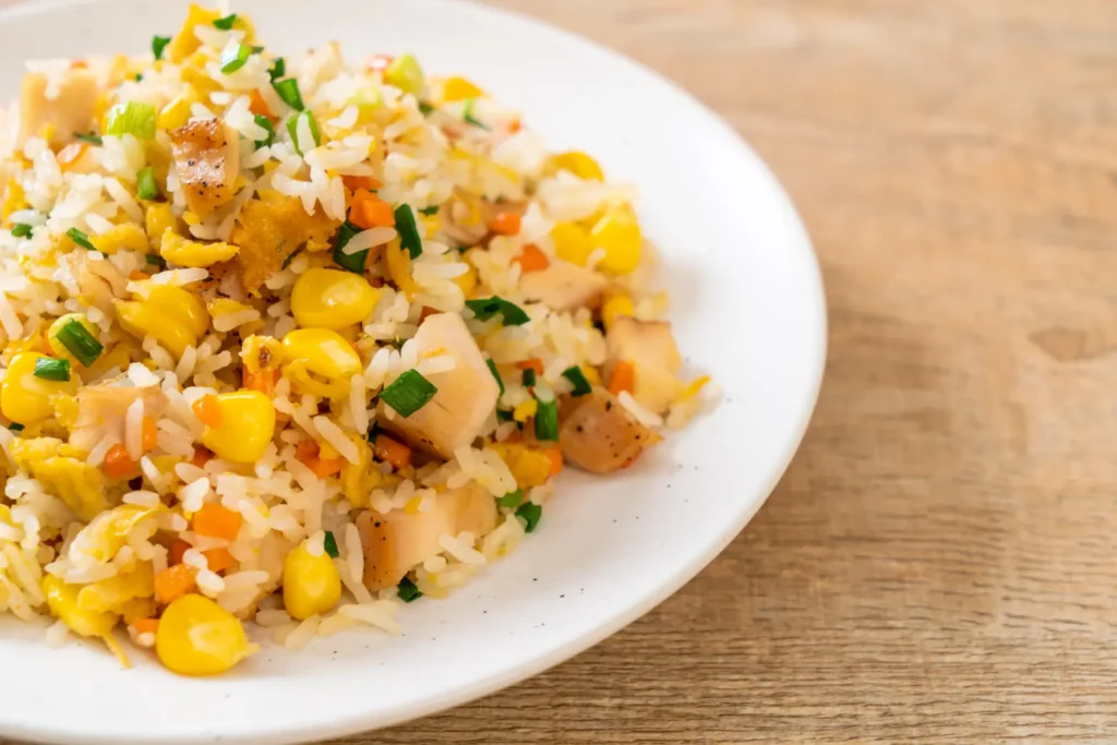 A plate of chicken fried rice with diced chicken, corn, carrots, and green onions, served on a white plate for a vibrant and satisfying meal.