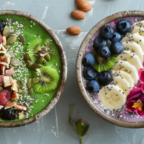 Two beautifully arranged smoothie bowls—one green and one purple—topped with fresh fruit, nuts, seeds, and edible flowers, served in rustic bowls on a textured surface.