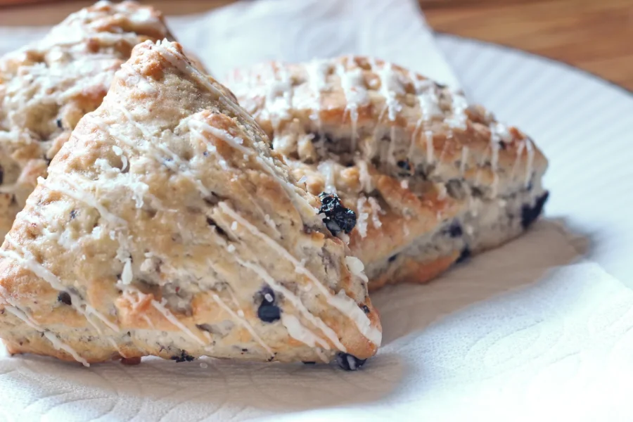 Freshly baked blueberry scones drizzled with white icing, served on a white plate with a napkin.