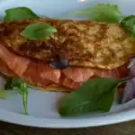 A golden-brown omelette filled with fresh smoked salmon and garnished with mixed greens on a white plate.