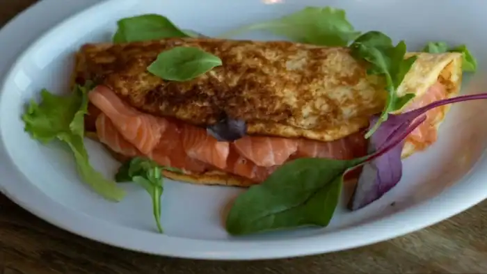 A golden-brown omelette filled with fresh smoked salmon and garnished with mixed greens on a white plate.