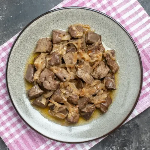 A plate of sautéed chicken livers with caramelized onions, served on a rustic dish over a checkered pink and white kitchen towel.