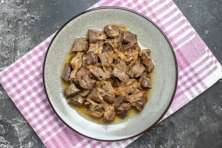 A plate of sautéed chicken livers with caramelized onions, served on a rustic dish over a checkered pink and white kitchen towel.