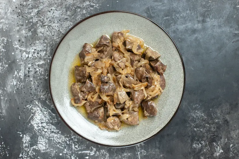 A plate of tender chicken livers cooked with caramelized onions, served on a rustic ceramic dish against a dark textured background.