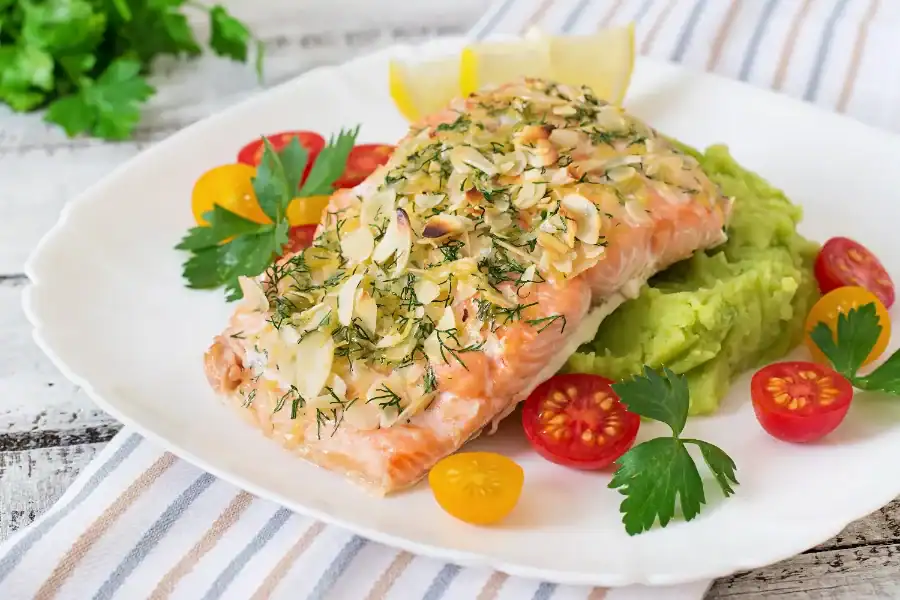 Baked salmon fillet with almond and herb crust served over mashed avocado with cherry tomatoes