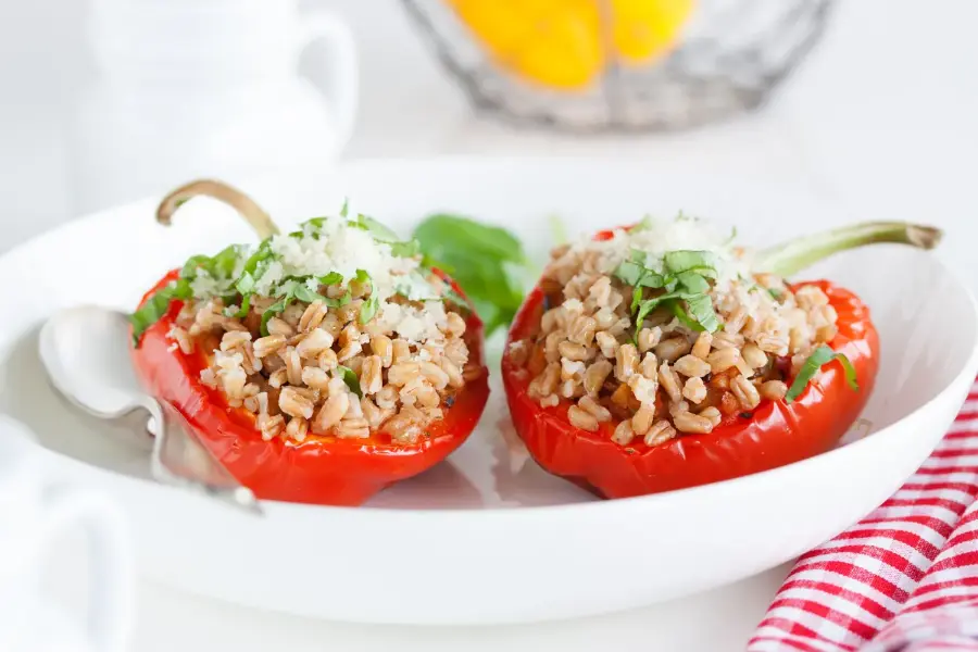 Red bell peppers stuffed with grains, topped with fresh herbs and cheese, served on a white plate.