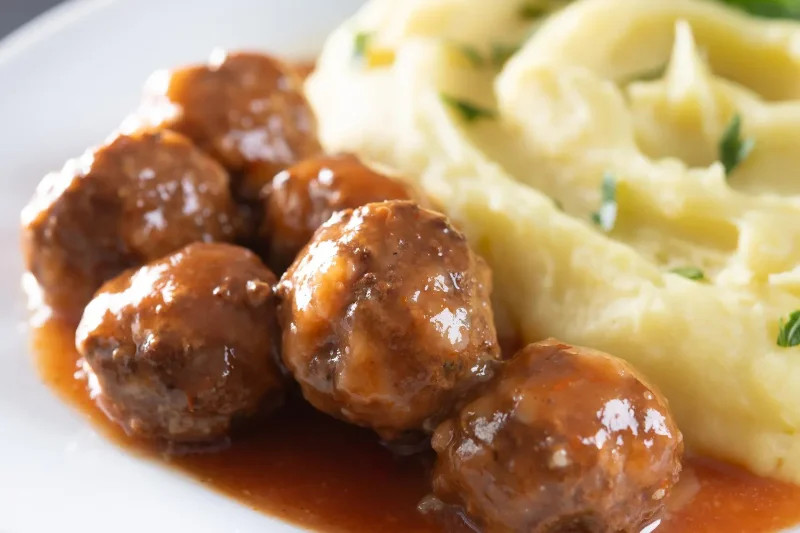 A plate of traditional Italian meatballs in rich tomato sauce served with creamy mashed potatoes, garnished with fresh parsley.