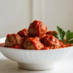 A white bowl filled with Italian meatballs in marinara sauce, garnished with fresh parsley.