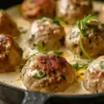 A close-up of Swedish meatballs in a creamy gravy, garnished with fresh herbs, served in a skillet.
