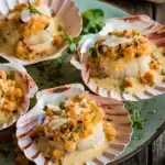 Garlic butter scallops in shell topped with herbs, breadcrumbs, and served with creamy sauce