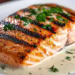 Grilled salmon fillet served with creamy herb sauce on a white plate