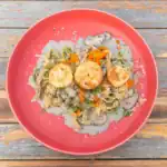 Top view of scallops pasta with truffle cream sauce, mushrooms, and herbs served on a red plate.