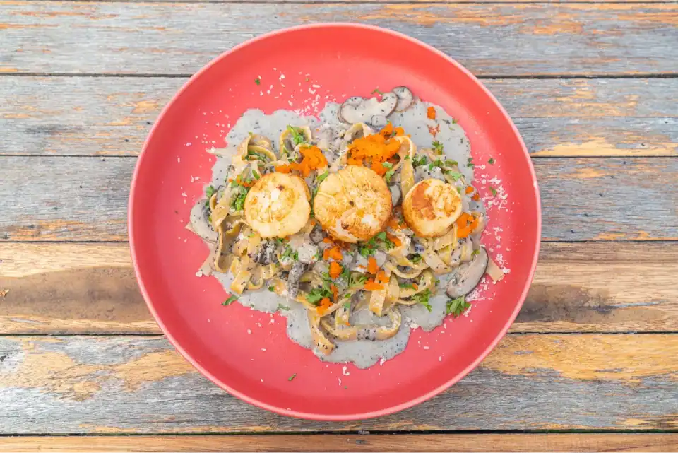 Top view of scallops pasta with truffle cream sauce, mushrooms, and herbs served on a red plate.