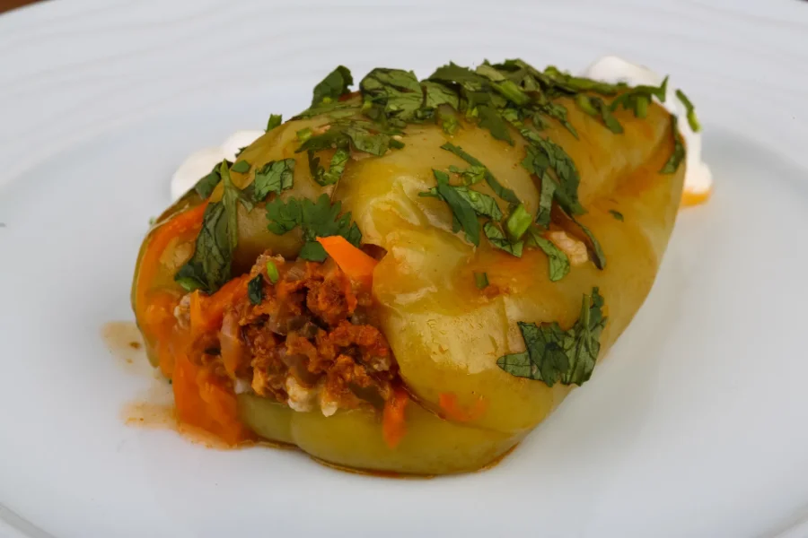 A green bell pepper stuffed with a savory mixture of meat, rice, and carrots, garnished with fresh chopped parsley and served on a white plate.