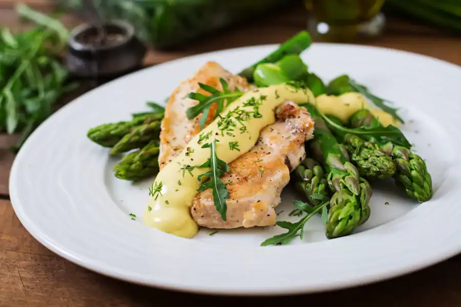 Grilled chicken breast served with fresh asparagus and creamy sauce on a white plate
