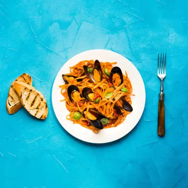 Spaghetti with mussels in red sauce served on a white plate with grilled bread