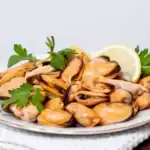 Cooked mussels without shells served on a plate with lemon and parsley