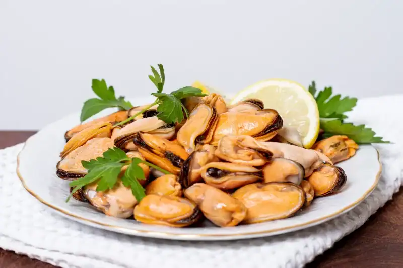 Cooked mussels without shells served on a plate with lemon and parsley