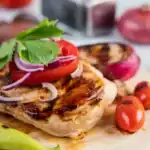 Grilled BBQ chicken breast topped with tomato, onion, and parsley, served with grilled vegetables.