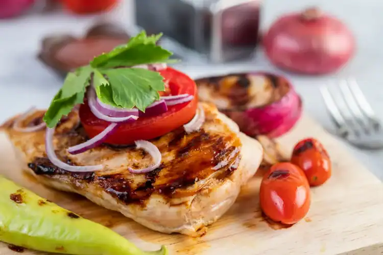 Grilled BBQ chicken breast topped with tomato, onion, and parsley, served with grilled vegetables.