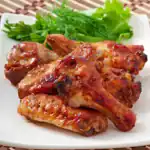 Sweet and spicy BBQ chicken drumsticks served on a white plate with fresh herbs