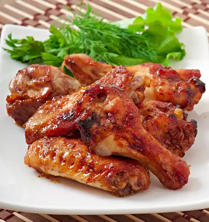 Sweet and spicy BBQ chicken drumsticks served on a white plate with fresh herbs