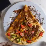 Crepe filled with fresh fruit and topped with melted chocolate and sprinkles