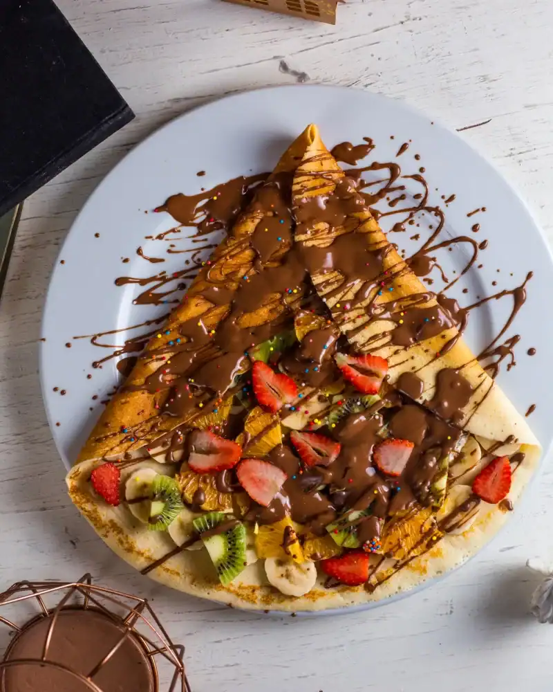 Crepe filled with fresh fruit and topped with melted chocolate and sprinkles