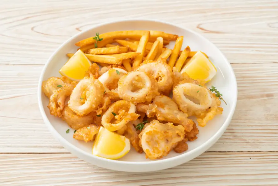 Crispy fried squid rings with French fries and lemon wedges on a white plate