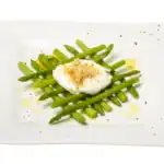 Steamed asparagus spears served with a poached egg and crispy croutons on a white plate.