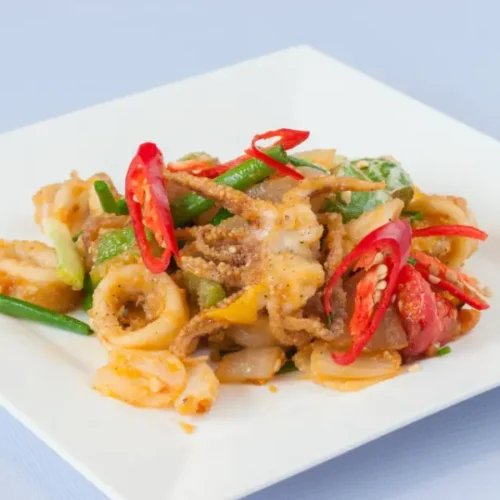 Fried squid with chili peppers, green beans, and vegetables on a square white plate