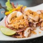 Grilled-style fried squid with garlic topping and lime wedge on a white plate