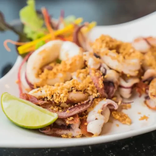 Grilled-style fried squid with garlic topping and lime wedge on a white plate