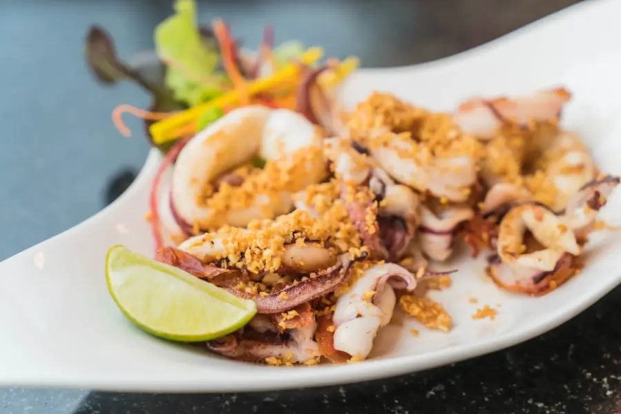 Grilled-style fried squid with garlic topping and lime wedge on a white plate