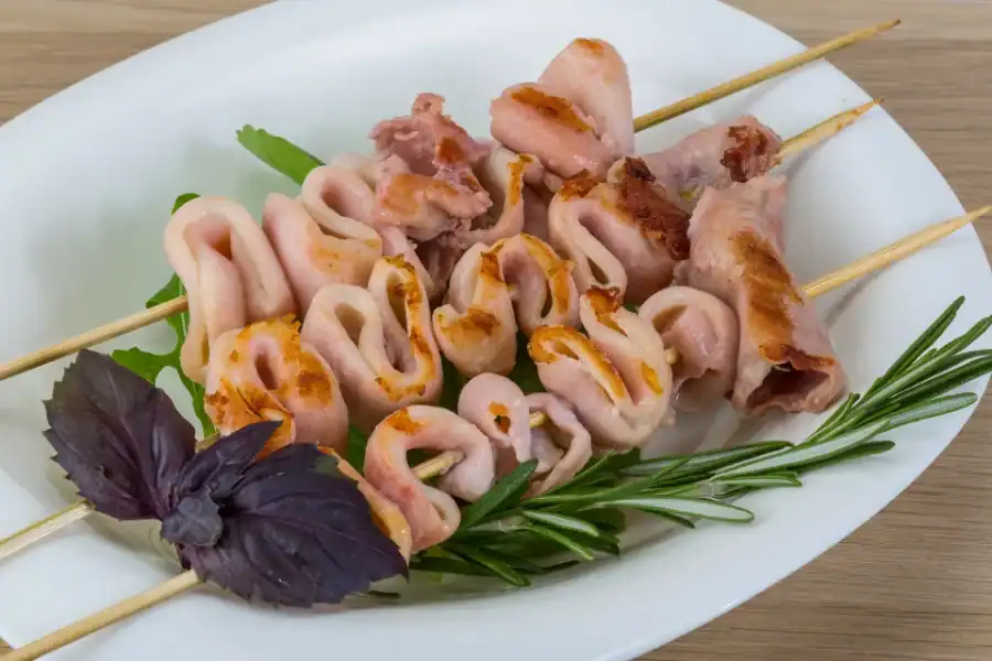 Grilled calamari skewers on a white plate with rosemary and fresh basil garnish