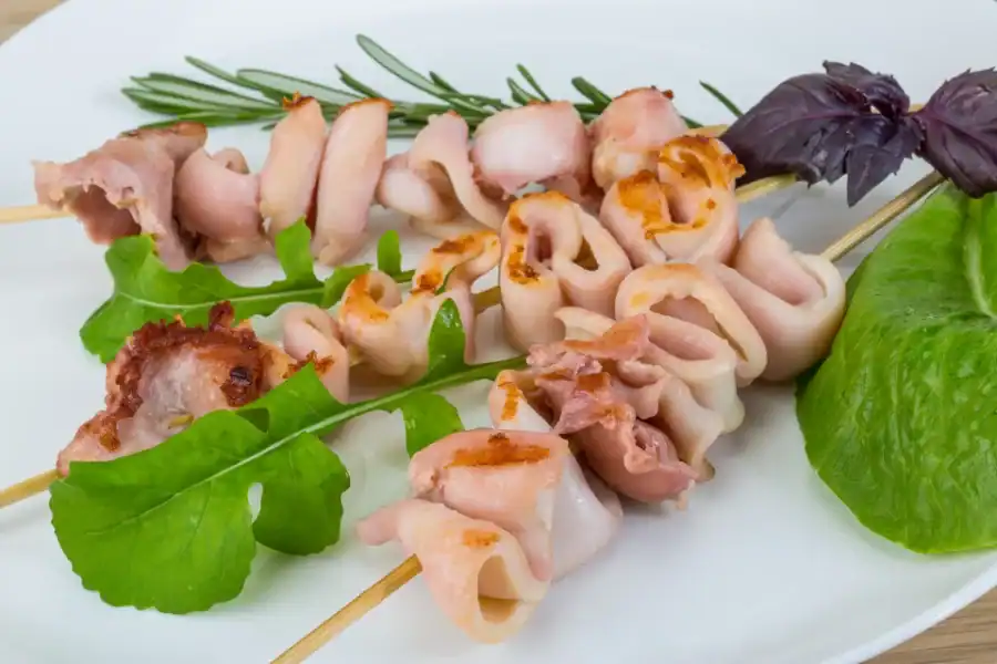 Grilled calamari skewers served with fresh greens and herbs on a white plate