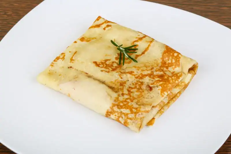 Folded savory crepe with rosemary garnish on a white plate
