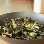 Thai-style mussels cooked with herbs, ginger, and vegetables in a large black wok
