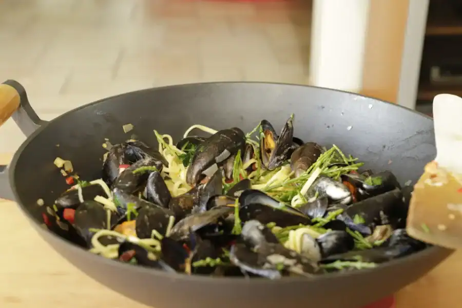 Thai-style mussels cooked with herbs, ginger, and vegetables in a large black wok