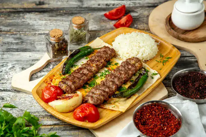Two Adana kebabs served on lavash with grilled vegetables and rice on a wooden platter