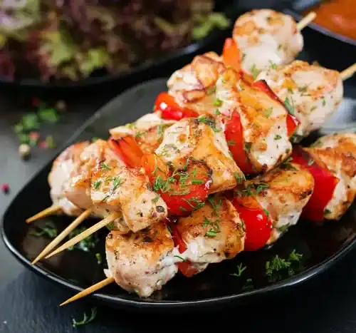 Grilled chicken kebabs with red bell peppers on skewers, served on a black plate